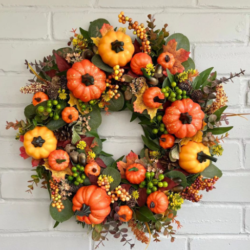 Pumpkin harvest wreath with orange and gold pumpkins, berries and autumn leaves on a white brick wall