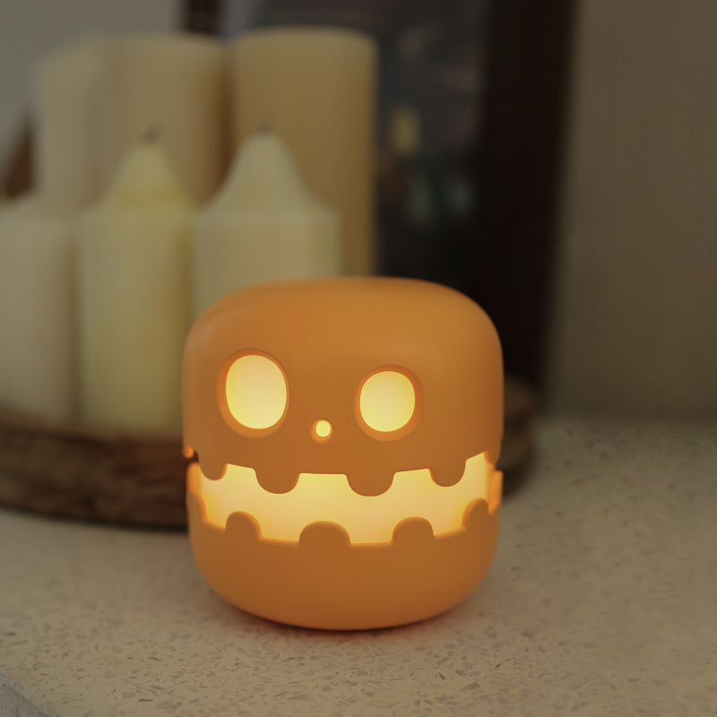Pumpkin night light glowing beside candles on a table