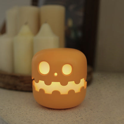 Pumpkin night light glowing beside candles on a table