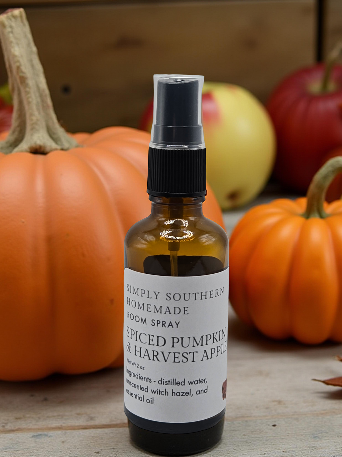 Spiced Pumpkin and Harvest Apple room spray in front of orange pumpkins and red apples