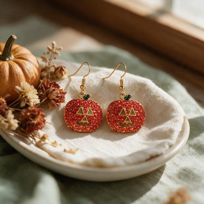 Red rhinestone jack-o-lantern earrings with gold hooks on a linen dish beside a mini pumpkin
