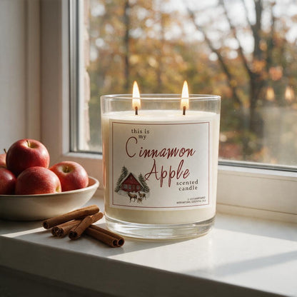 Lit 2-wick Cinnamon Apple soy candle on a kitchen windowsill with a bowl of red apples and cinnamon sticks