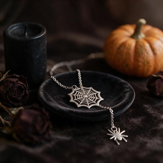 Silver spider web pendant necklace with hanging spider on a black velvet dish