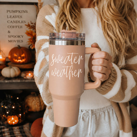 Woman holding the peach Sweater Weather 40 oz tumbler in a cozy fall room