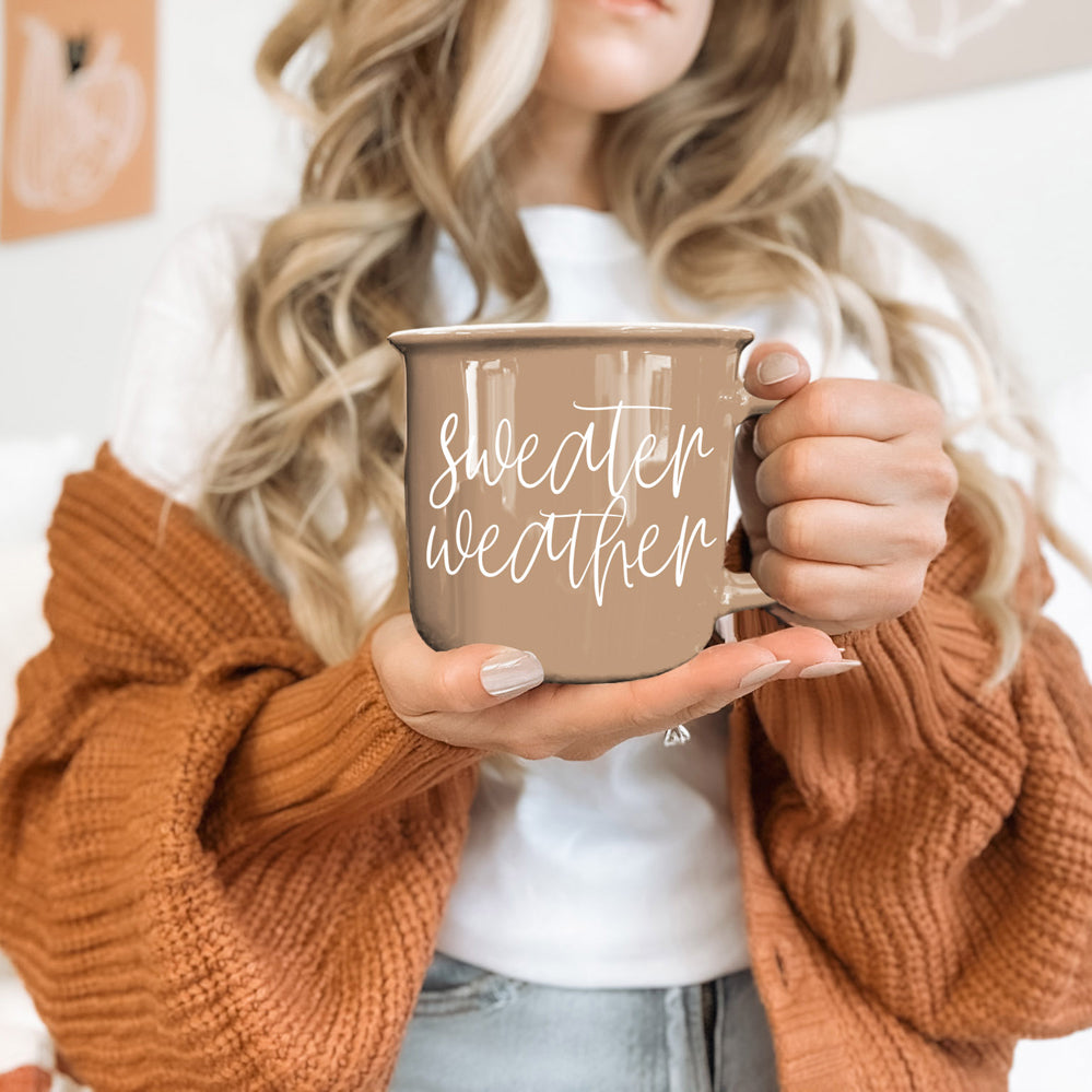 Woman in a rust cardigan holding the Sweater Weather mug