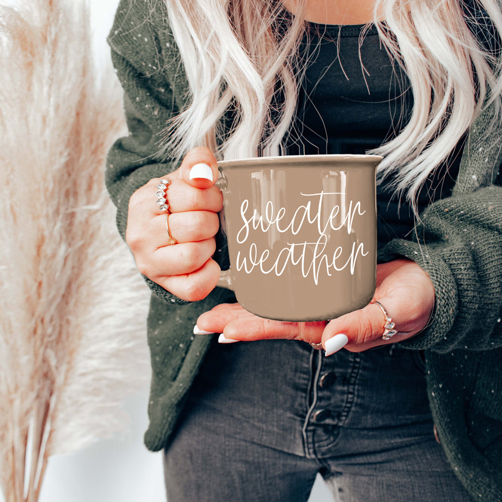 Woman in a green cardigan holding the tan Sweater Weather mug