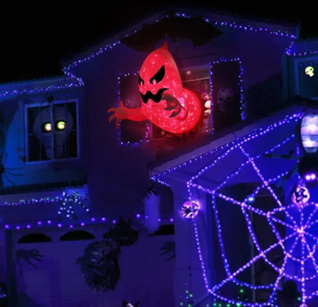 Red inflatable ghost bursting from an upstairs window of a house lit for Halloween