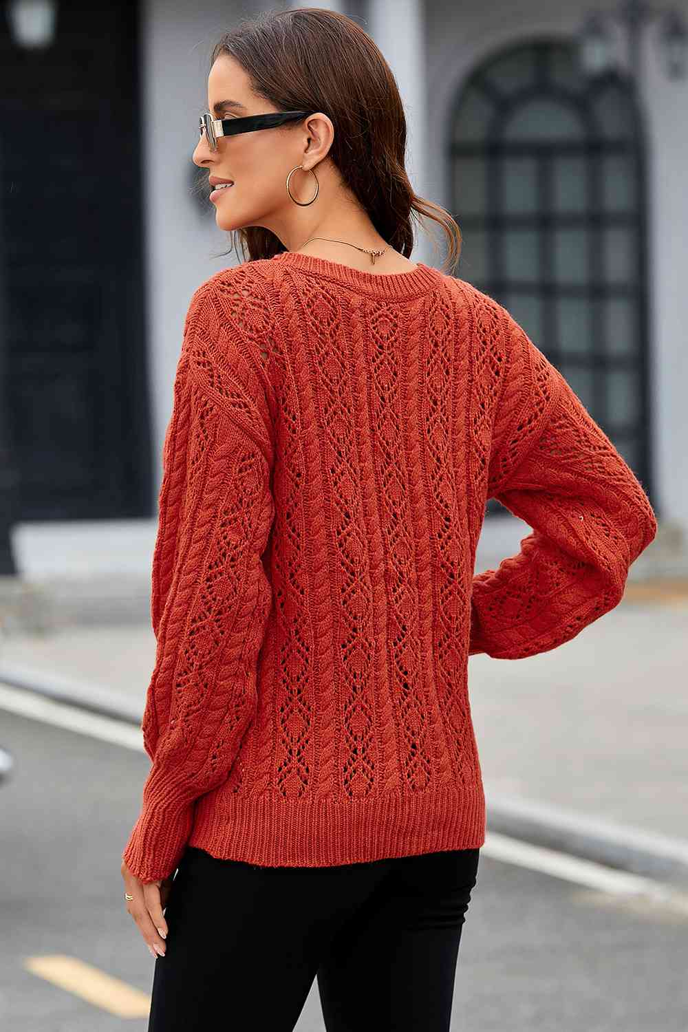 Back view of the brick red cable-knit pullover sweater with black pants