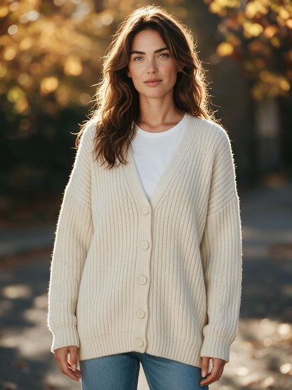 Woman wearing the beige chunky ribbed knit sweater cardigan buttoned over a white tee with jeans in autumn light