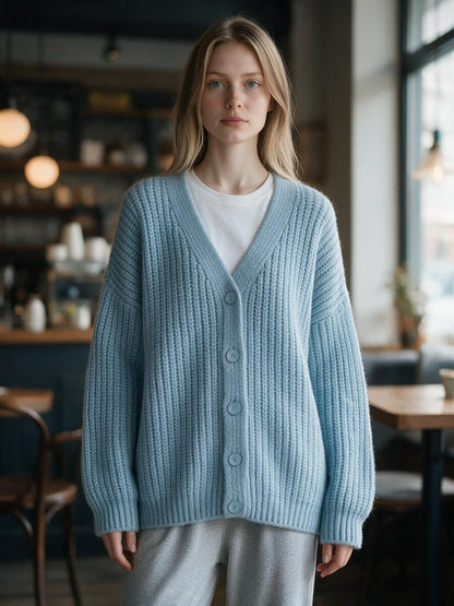 Woman wearing the sky blue chunky ribbed knit sweater cardigan over a white tee in a cozy cafe